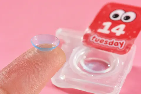 a daily lens on a fingertip next to its tuesday blister, numbered 14